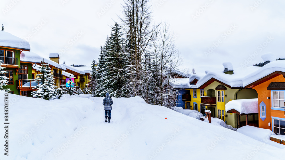 Fototapeta premium Walking through the snow along the colorful houses in the Village of Sun Peaks, an Alpine Village in the Shuswap Highlands of British Columbia, Canada