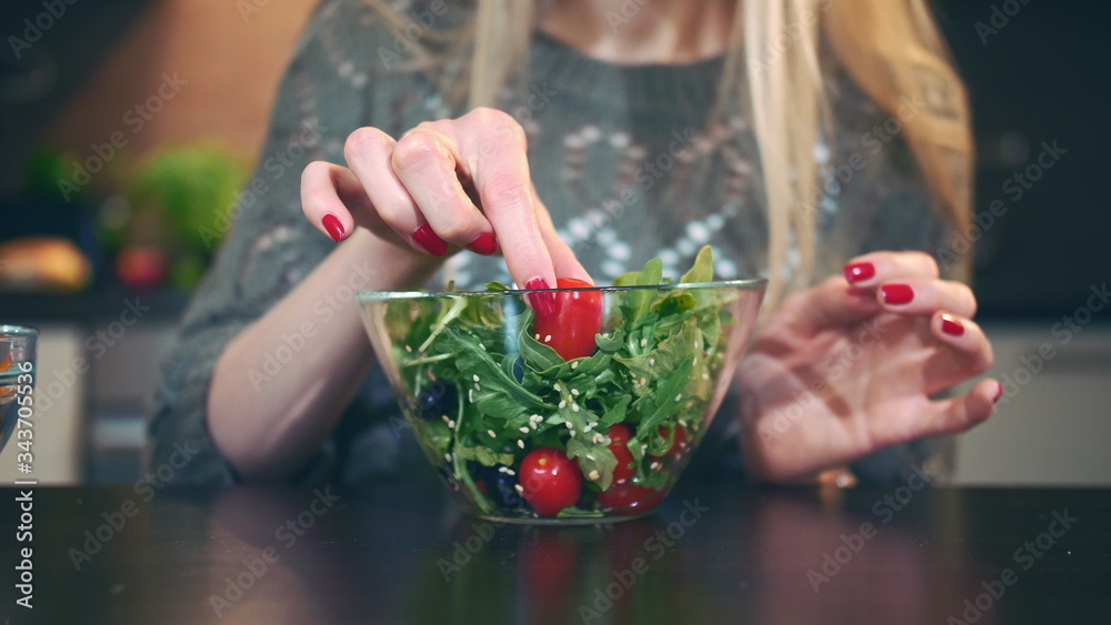 Close-up shot of Young lady preferring salad. Beautiful young woman choosing to eat healthy crisp for supper while sitting at table in stylish kitchen and she eats these salad.