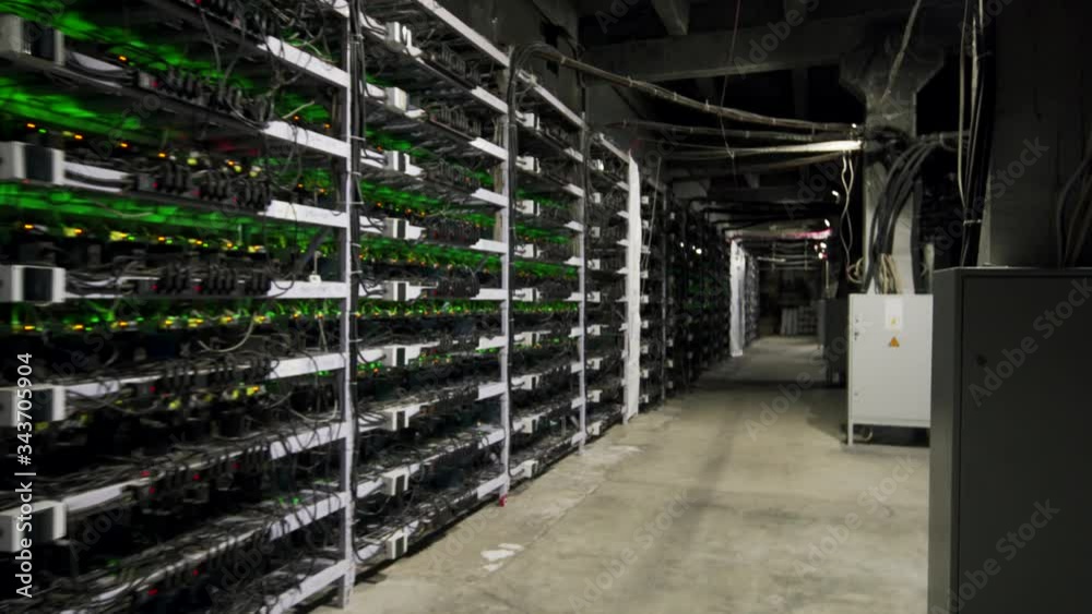 Cryptocurrency mining equipment on large farm. ASIC miners on stand racks mine bitcoin in server room. Blockchain techology application specific integrated circuit. Steadycam footage along racks.