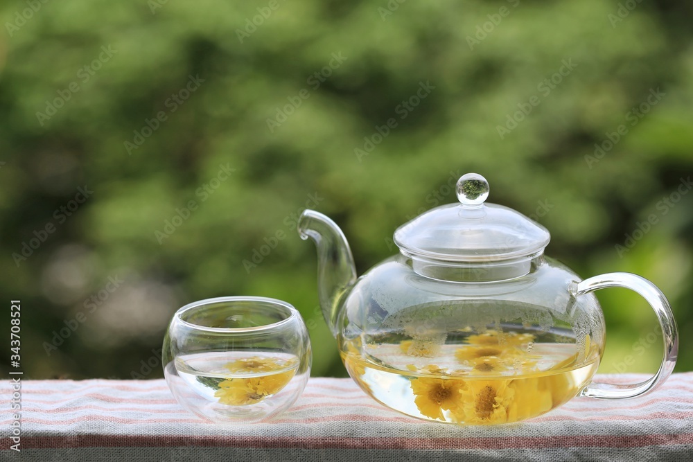 Chrysanthemum tea in glass teapot on blurred natural background Chrysanthemum tea in glass teapot on blurred natural background
