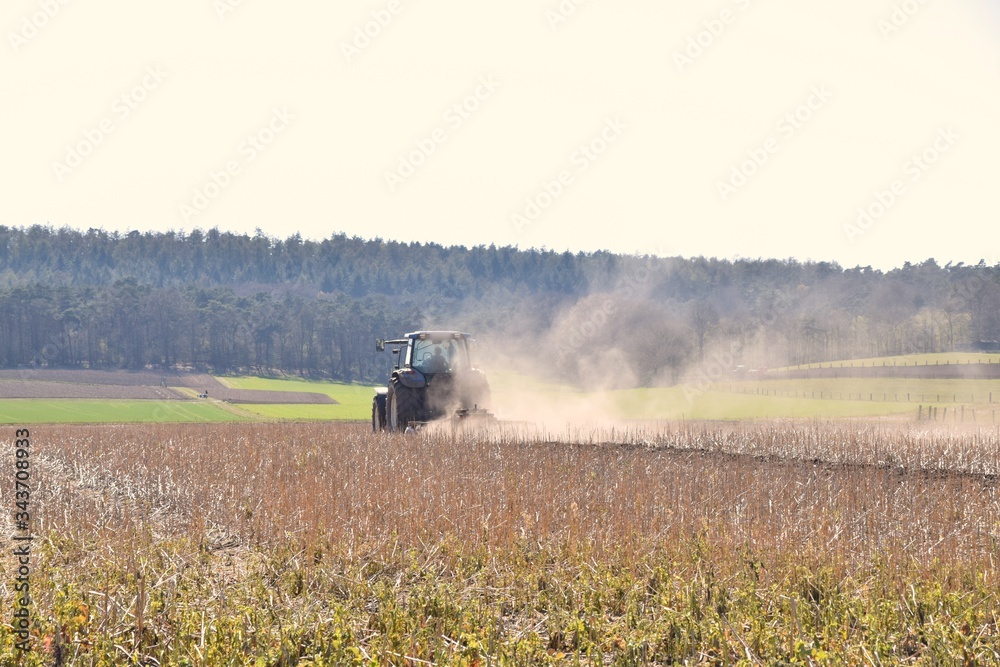 Fototapeta premium Bauer pflügt mit Traktor ein Feld in großer Hitze