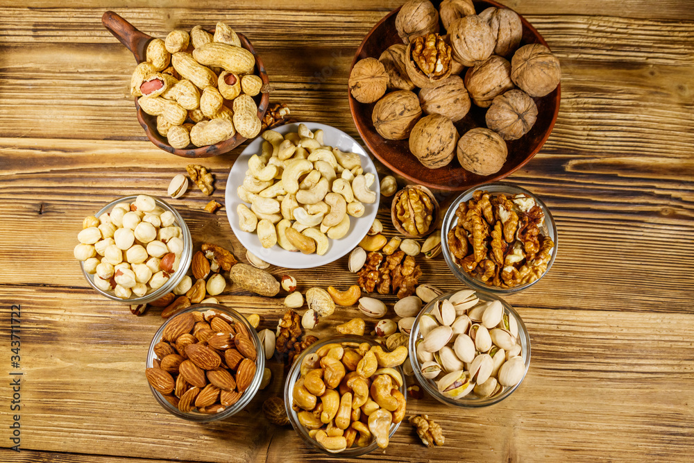 Fototapeta premium Assortment of nuts on wooden table. Almond, hazelnut, pistachio, peanut, walnut and cashew in small bowls. Top view. Healthy eating concept