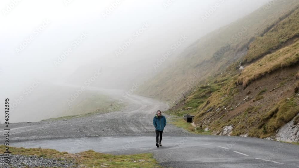 Young Man Walks Up Rainy Road In Hills