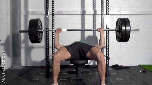 A male fitness model performs a bench press with a heavy weight loaded barbell. Slow motion. photo