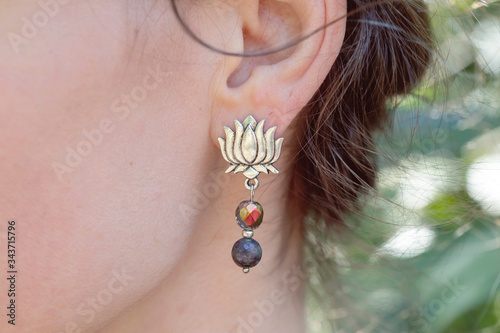 Outdoor detail of female ear wearing beautiful elegant earring in the shape of the lotus