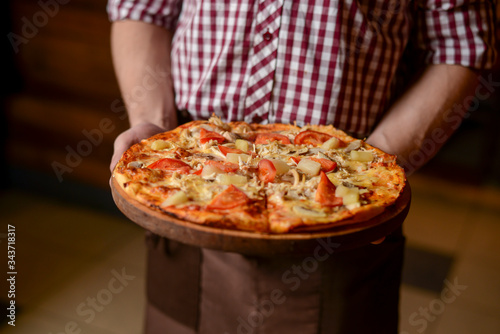 A waiter holds a plate of tasty food. Italian cuisine in restaurant, Delicious pizza with spinach, olives and mushrooms