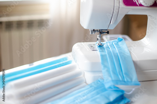 Hand-stitched medical masks, cloth spunbond, sms, Meltblown and sewing machine in room at home against background of window. Hand-made coronavirus protection. photo