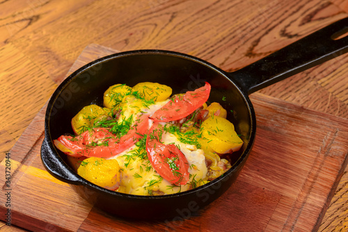 Roasted potato with tomatoes and dill in a frying pan on wooden table. Tasty delicious dinner.