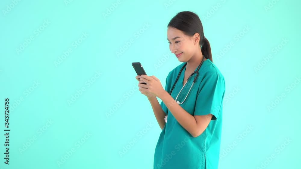 A young isolated asian nurse or a doctor using her mobile phone on green plain background. A young isolated asian nurse or a doctor using her mobile phone on green plain background.