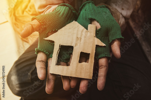Fotografie The dirty homeless man in his hand has a house made of brown cardboard, an impossible hope