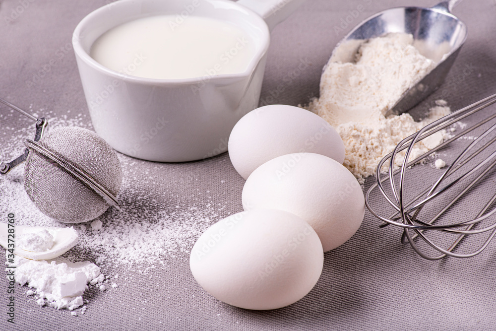 in the kitchen on the background of gray cloth, in the foreground, some utensils, flour, milk and eggs for the preparation of homemade culinary recipes in the kitchen on the background of gray cloth, in the foreground, some utensils, flour, milk and eggs for the preparation of homemade culinary recipes