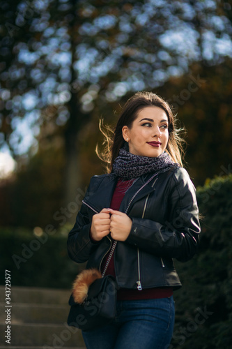 Stylish beautiful lady in a black leather jacket with a black bag and burgundy blouse. Attractive young woman smile