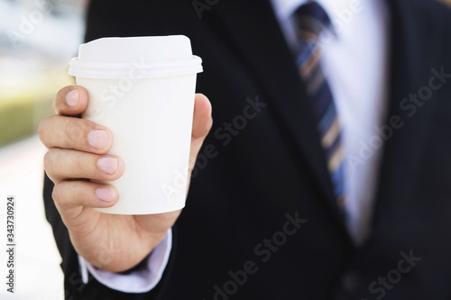 beverage. businessman hand holding paper cup of take away drinking coffee  on natural morning sunlight. space Place for your text or logo. 