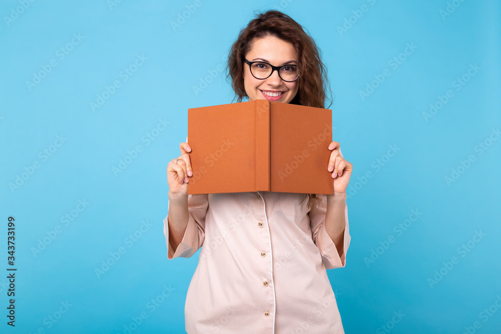 Smiling young girl in pajamas home wearis reading a book on blue background studio portrait. Relax good mood lifestyle concept. Smiling young girl in pajamas home wearis reading a book on blue background studio portrait. Relax good mood lifestyle concept.