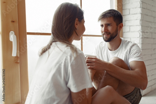 Cute couple in a bedroom. Lady in a white t-shirt. Pair sitting on a windowsill.