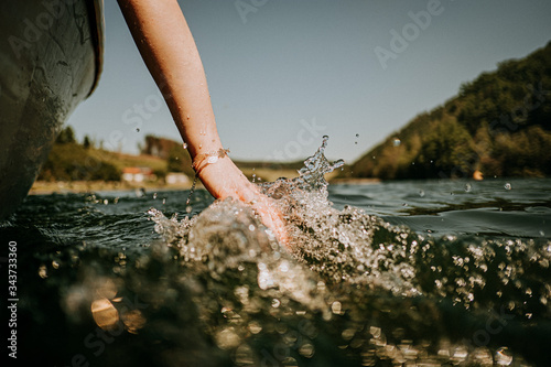 woman on boat is holding hand in water with splashing waves
