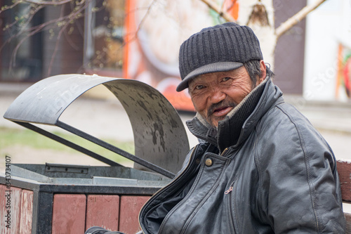 A poor homeless man is sitting on a bench on a city street