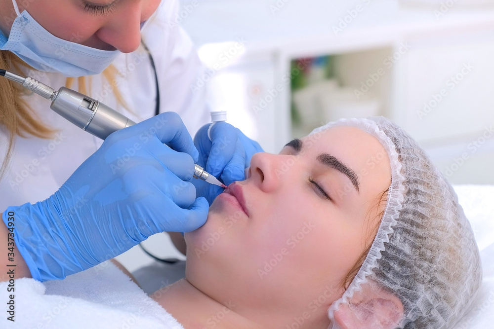 Cosmetologist making lips microblading procedure for girl using tattoo machine, face closeup. Beautician is applying permanent makeup on woman's lips. Beauty industry concept. Painting lips contour. Cosmetologist making lips microblading procedure for girl using tattoo machine, face closeup. Beautician is applying permanent makeup on woman's lips. Beauty industry concept. Painting lips contour.