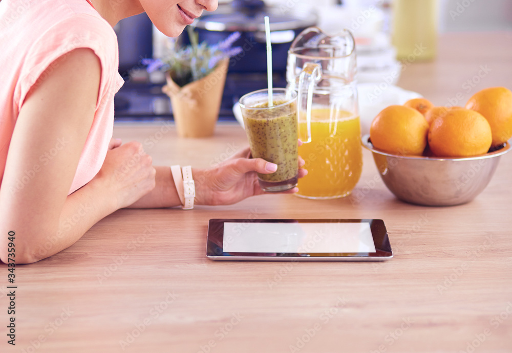 Beautiful young woman using a digital tablet in the kitchen.