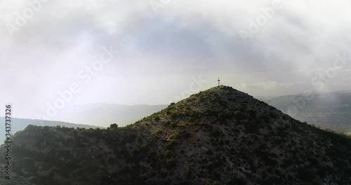 aerial dolly in towards cross in the rugged green mountain ranges, foggy day photo