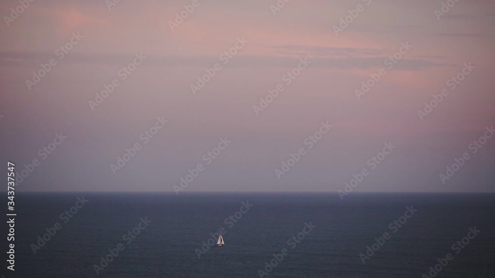Panoramic seascape view of a sailboat slowly moving, at sunset