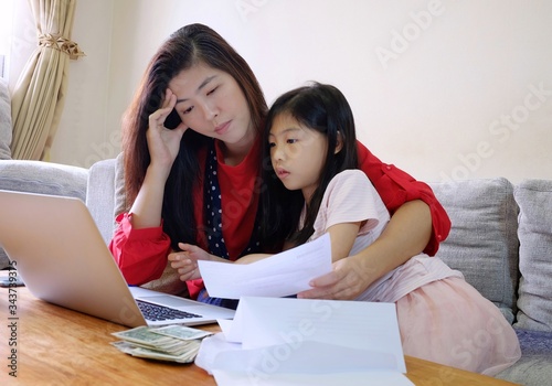 An attractive Asian woman working from home during corona virus outbreak, stress over her work and bills with her pretty young daughter enjoying her time with her mother.