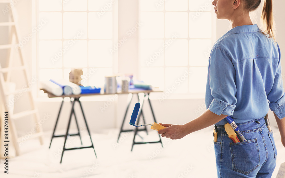 Pretty smilling woman painting interior wall of home with paint roller Pretty smilling woman painting interior wall of home with paint roller