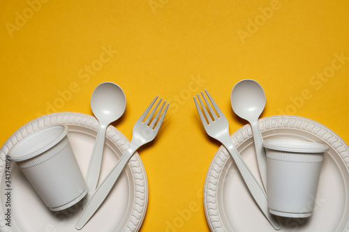 Tableau sur toile two sets of disposable spoons, forks, plates and glasses of corn starch on a yellow background