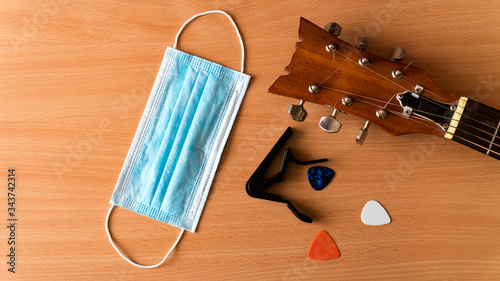 Acoustic guitar, capo, pick and blue medical mask lie on a wooden background. Coronavirus epidemic music concept with copy space.