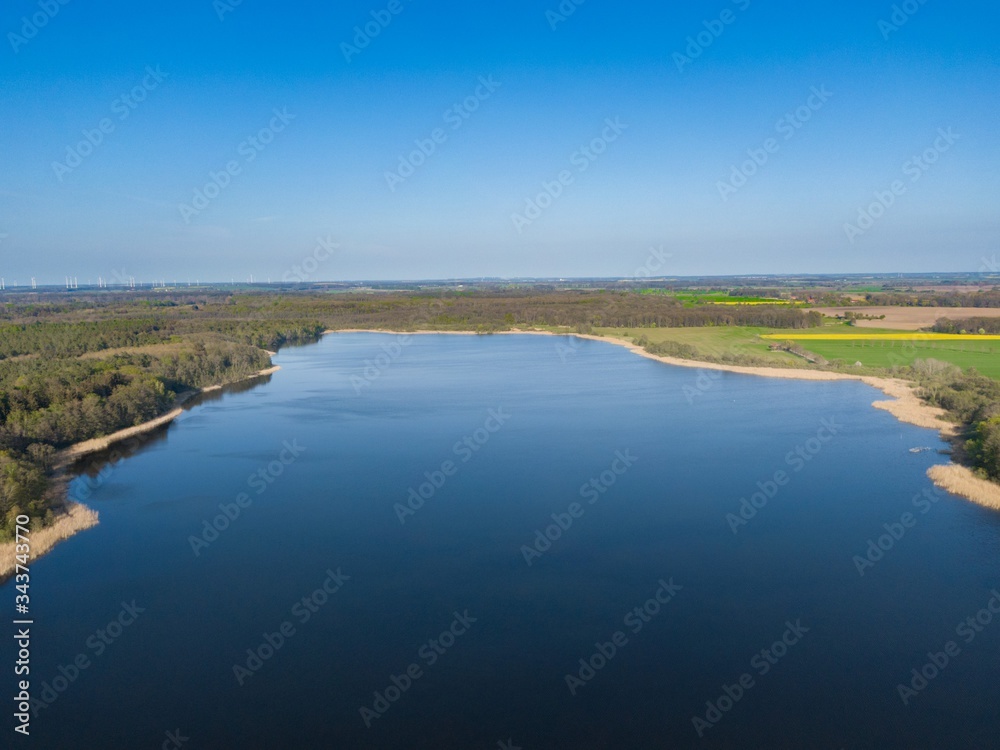 aerial view of a big blue lake with blue sky surrounded by green trees in a rural area