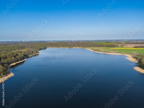 aerial view of a big blue lake with blue sky surrounded by green trees in a rural area