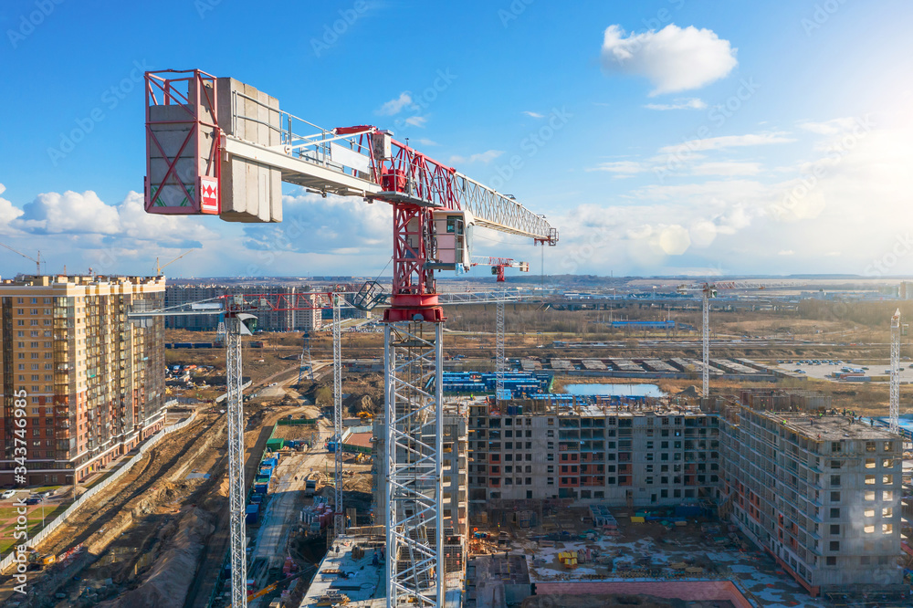 Construction cranes erected a multi-storey building with apartments on a background of blue sky with clouds, aerial drone view.