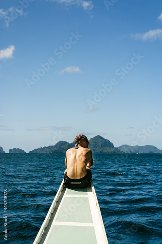Man sitting on his back on the bow of a traditional Filipino boat on an island hopping in El Nido, Palawan, Philippines