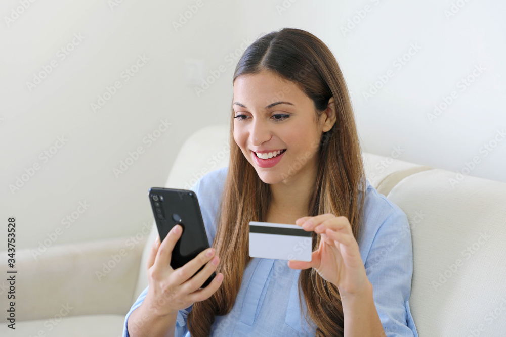 Lady buying online with a credit card and smart phone sitting relaxed on a couch in her living room at home Lady buying online with a credit card and smart phone sitting relaxed on a couch in her living room at home