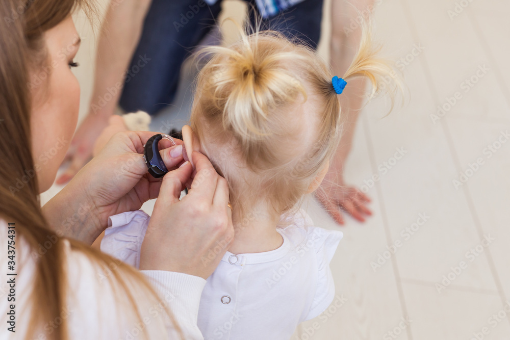 Fototapeta premium Hearing aid in baby girl's ear. Toddler child wearing a hearing aid at home. Disabled child, disability and deafness concept.