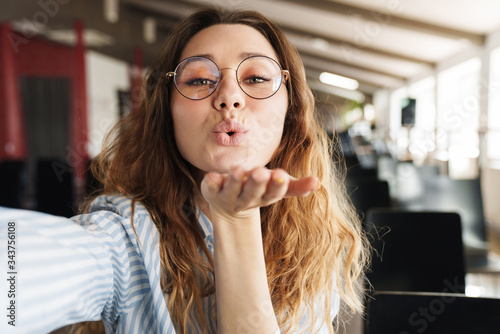 Valokuva Image of happy beautiful woman blowing air kiss and taking selfie photo