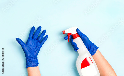 Hands in rubber medical gloves holds a bottle with antiseptic spray on a blue background.