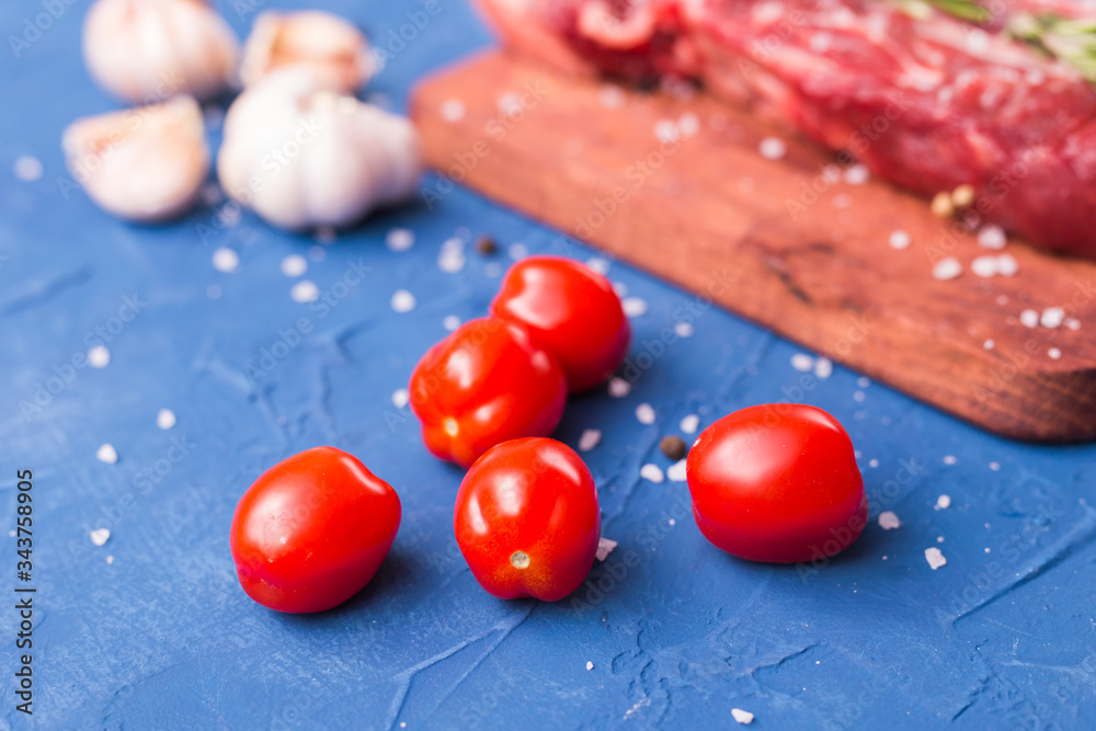 Close-up of fresh small tomatoes on blue background. Ingredients for cooking meat.