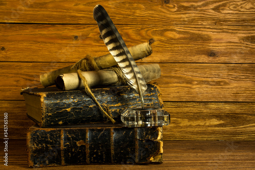 Two old big books, glass inkwell with a colorful pen, documents in scrolls on a wooden table.