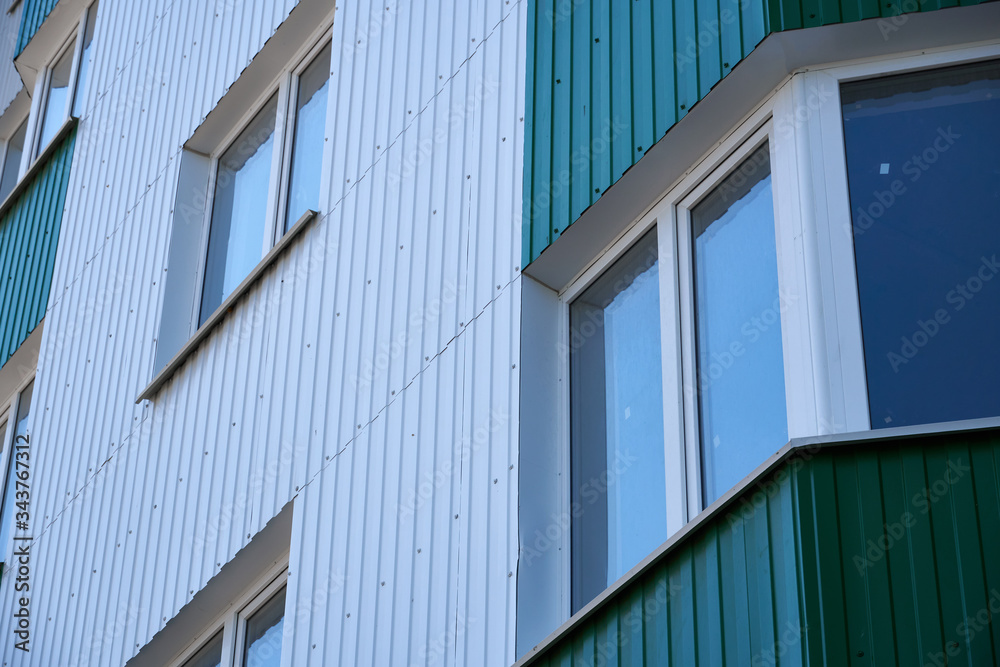 facade of a new multi-storey building with white and green metal siding, many Windows