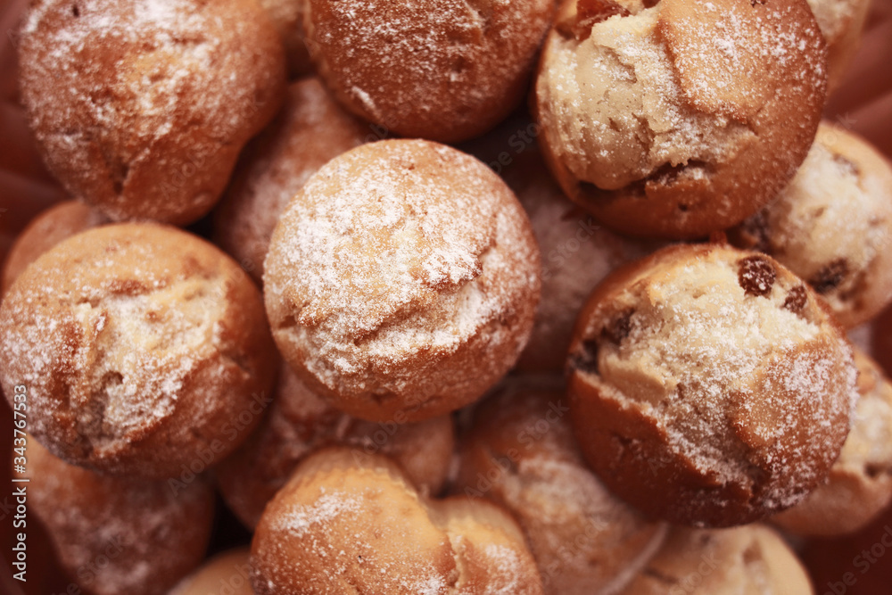 Delicious English muffins with raisins sprinkled with icing sugar. Cupcakes with biscuit air pastry and dried grapes. Hill of ruddy baked homemade sweet buns. Close-up, selective focus. Yummy cookies.