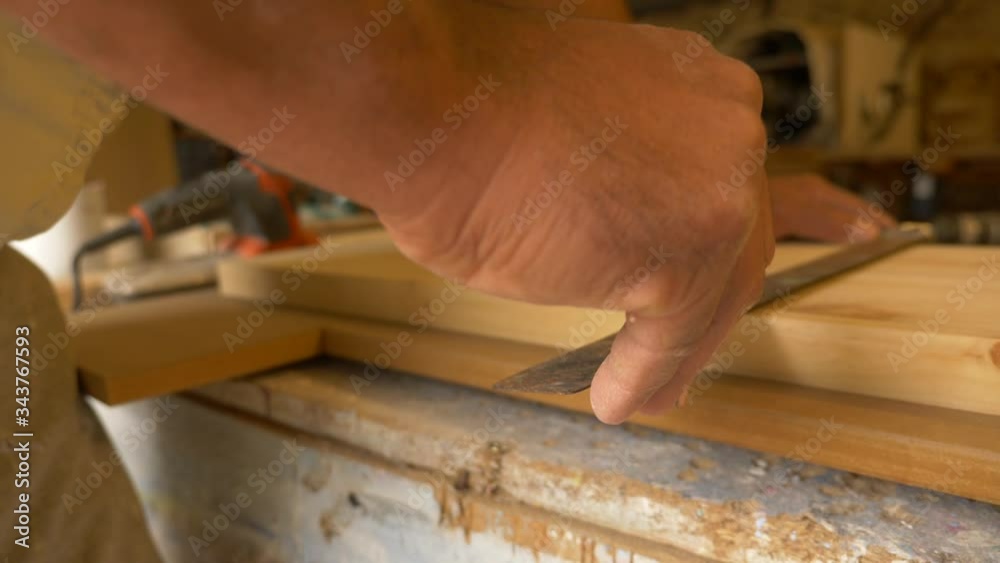 Carpintero sostiene una tabla de madera sobre la mesa de trabajo mientras dibuja una línea con un lápiz en la tabla con la ayuda de una escuadra en su taller de carpintería. Carpintero sostiene una tabla de madera sobre la mesa de trabajo mientras dibuja una línea con un lápiz en la tabla con la ayuda de una escuadra en su taller de carpintería.