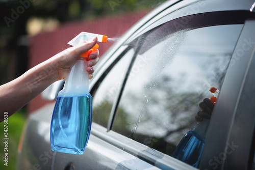 Cleaner is cleaning a car window glass with a rag and detergent close up.