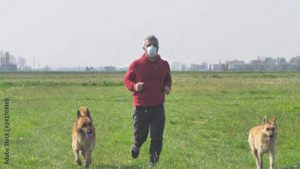 social distancing middle-aged caucasian man jogging wearing a protective mask,run outdoor in the countryside with his dogs social distancing middle-aged caucasian man jogging wearing a protective mask,run outdoor in the countryside with his dogs