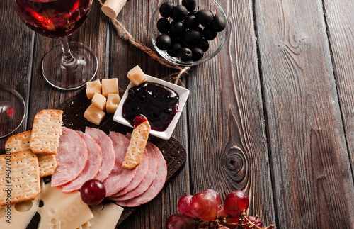 snack with red wine, slices of cheese , cracker, ham, olives, jam, grapes, baguette on a dark wooden , copy space,