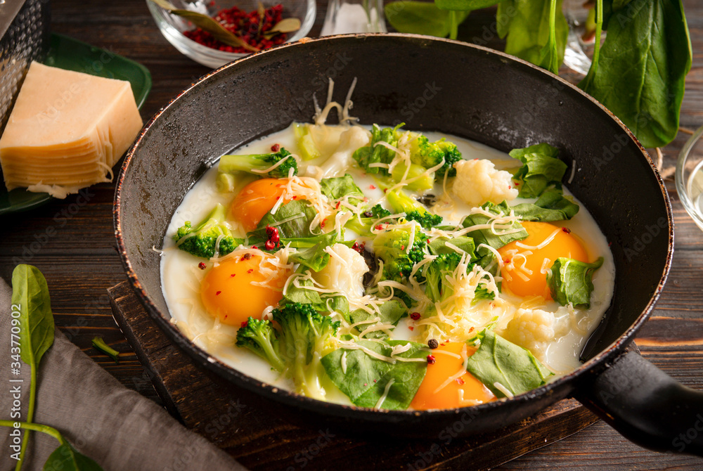 eggs with cheese, broccoli, spinach in a pan on a dark wooden background, delicious healthy Breakfast eggs with cheese, broccoli, spinach in a pan on a dark wooden background, delicious healthy Breakfast