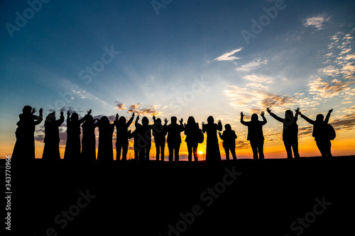 a group of people meets the dawn of the sun raising their hands up to the sun rays and the blue sky with clouds, dark silhouettes of people facing the Sun raised their hands at dawn