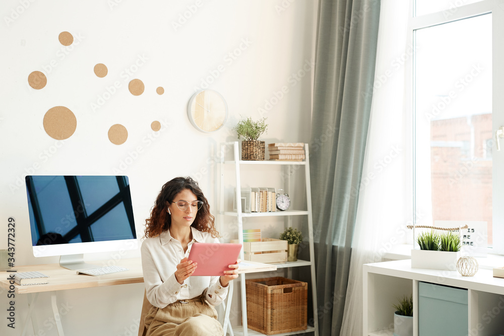 Young female remote worker sitting on chair in her room taking part in online meeting using her tablet computer