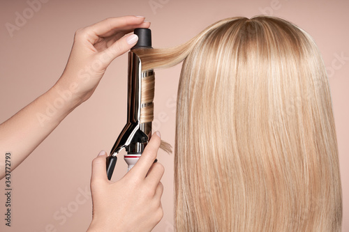 The hairdresser curls long hair with a Curling iron. Beautiful woman with long straight hair. Smooth hairstyle