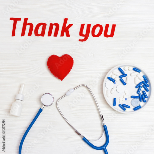 Flat lay with medical stethoscope, pills and text "thank you" on white wooden background with copy space. Words of gratitude for medical personnel. Top view.